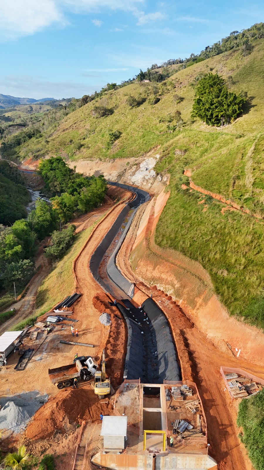 Canal de adução com geomembrana instalada e ancorada nas bordas do talude, obra em andamento — SPE Paquequer, Sumidouro/RJ